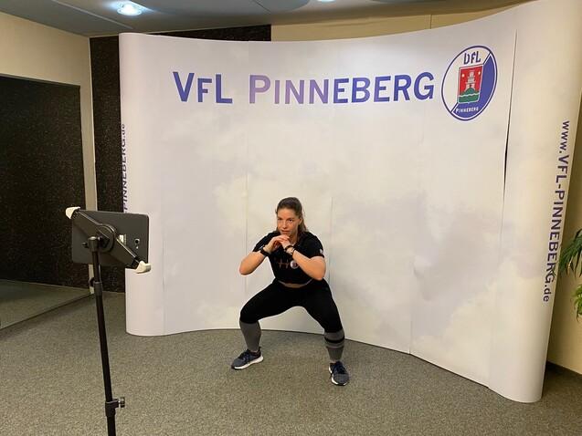Frau in Sportkleidung führt eine Kniebeuge vor einem Hintergrund mit dem Logo von VfL Pinneberg aus.