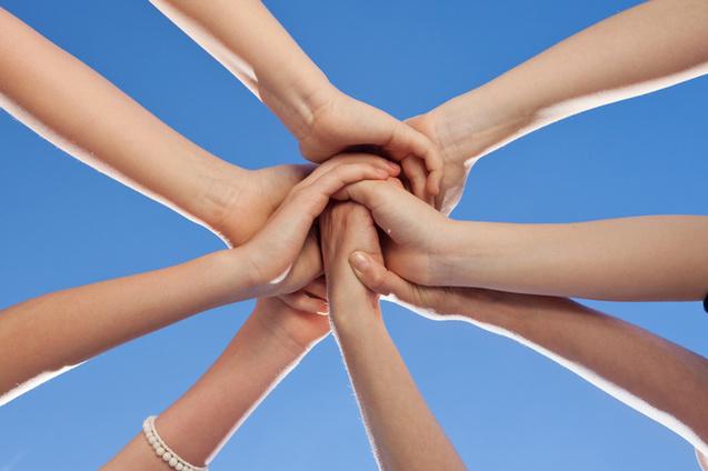 H&auml;nde verschiedener Personen ber&uuml;hren sich in der Mitte, vor blauem Himmel sichtbar.