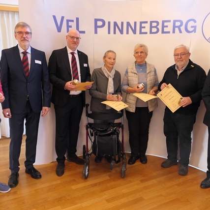 Gruppenszene mit sieben Personen vor einem VFL Pinneberg Banner, einige halten Urkunden und einen Ball.