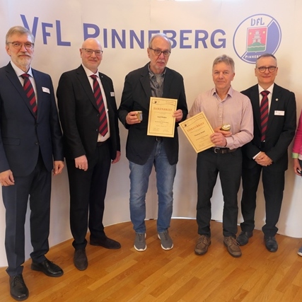 Sechs Personen stehen lächelnd vor einem Banner des VfL Pinneberg, einige halten Urkunden und Auszeichnungen in den Händen.