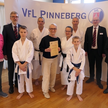 Gruppe von Personen in Karateuniformen und Anzug, posierend vor einem Banner des VfL Pinneberg. Eine Person hält eine Auszeichnung.