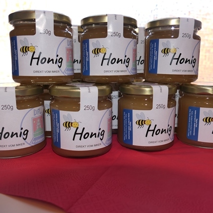 Mehrere Honiggläser mit Etiketten auf einem Tisch, teilweise auf einem roten Tuch gestapelt.