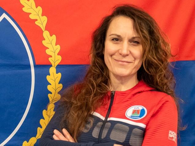 Frau mit lockigem Haar in Sportjacke, lächelt vor einer großen Flagge mit dem Wappen von Pinneberg.