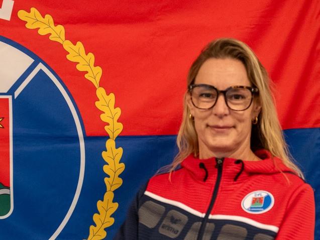 Frau mit Brille steht vor einer Flagge des DPL Pinneberg, die ein Wappen mit Turm und Sternen zeigt.