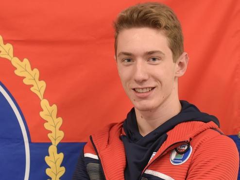 Junger Mann in roter Sportjacke mit blauem Hoodie steht vor einer roten Flagge mit dem Wappen von Pinneberg.