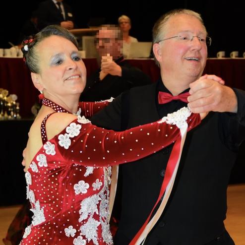 Tanzpaar in eleganten Outfits, sie tanzen gemeinsam in einem festlichen Saal. Die Frau trägt ein rotes, glitzerndes Kleid.
