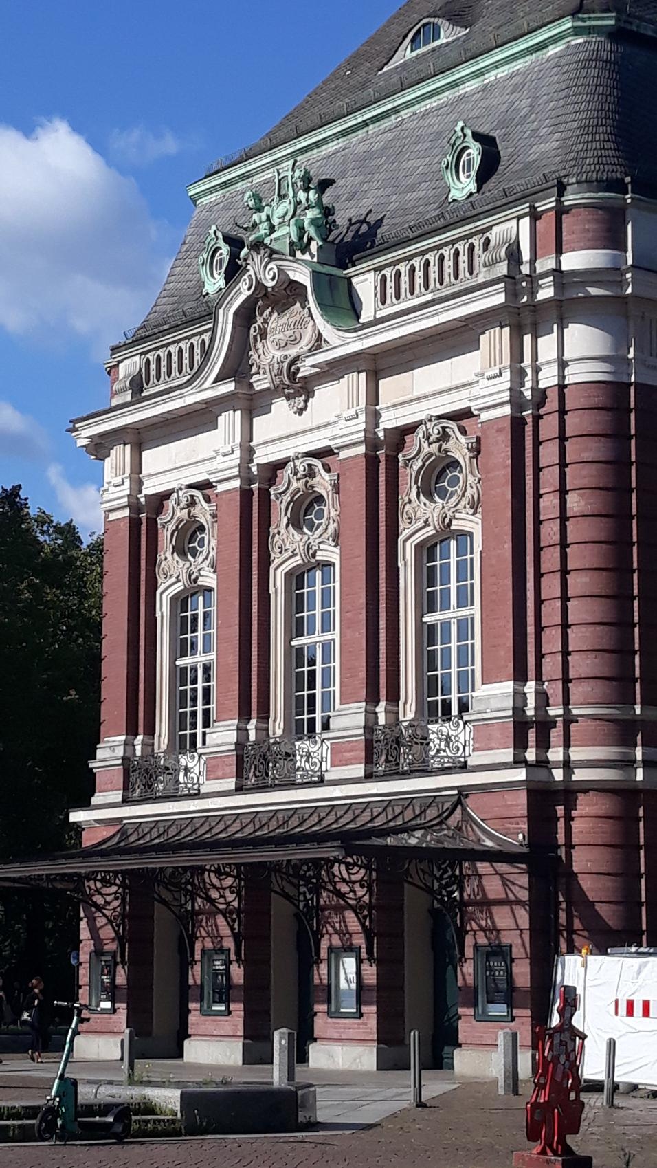 Historisches Gebäude mit charakteristischer Fassade, kunstvollen Fenstern und verziertem Dach unter blauem Himmel.