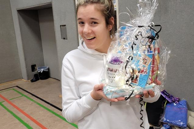 Junge Frau in Sportkleidung l&auml;chelt und h&auml;lt ein mit Geschenkpapier verpacktes Pr&auml;sent in der Hand.