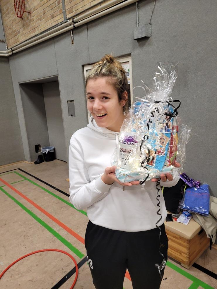 Junge Frau in Sportkleidung lächelt und hält ein mit Geschenkpapier verpacktes Präsent in der Hand.