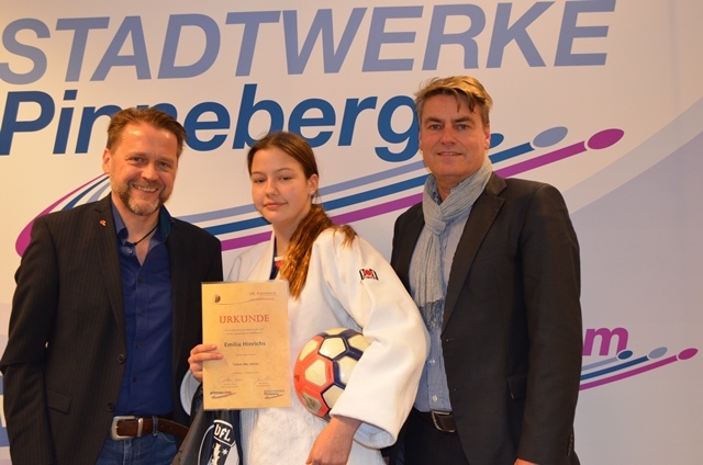 Drei Personen stehen vor einem Banner der Stadtwerke Pinneberg, ein Mädchen hält eine Urkunde und einen Fußball.