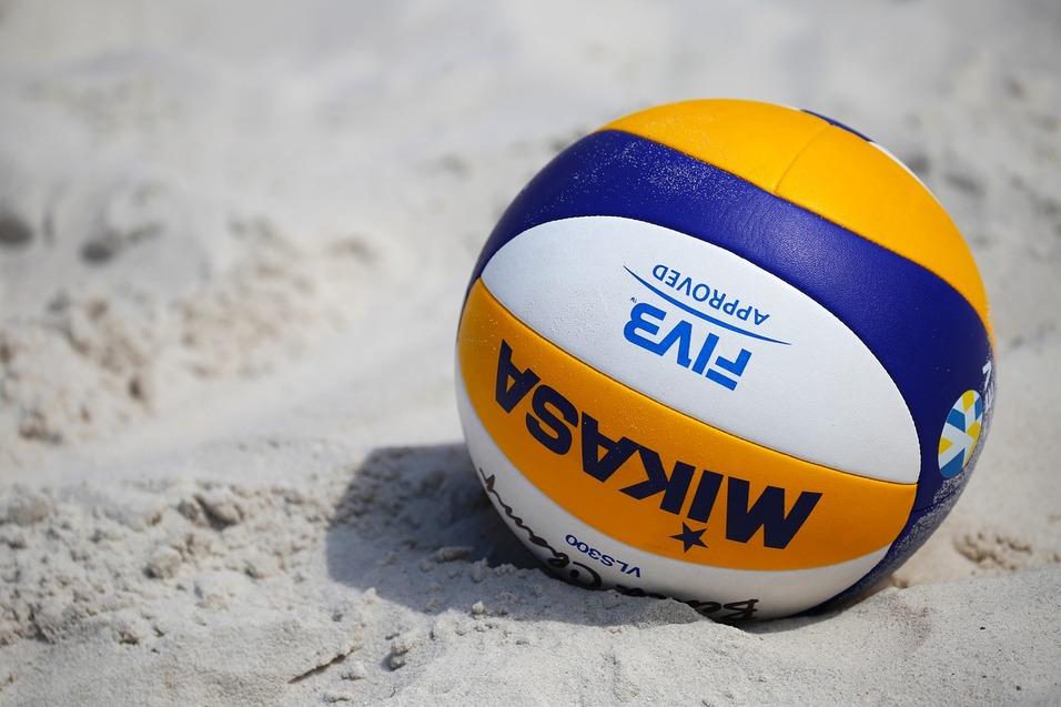 Nahaufnahme eines Volleyballs mit blau-gelber Farbgebung, teilweise im Sand liegend.
