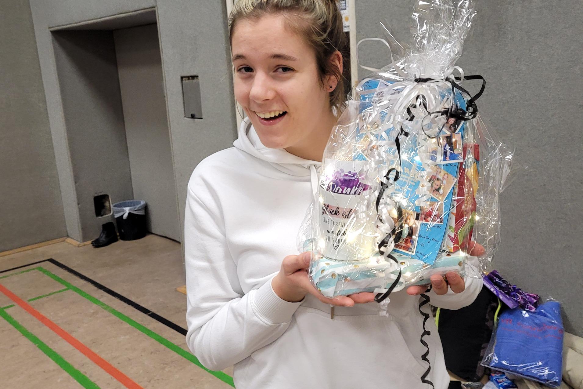 Junge Frau in Sportkleidung l&auml;chelt und h&auml;lt ein mit Geschenkpapier verpacktes Pr&auml;sent in der Hand.