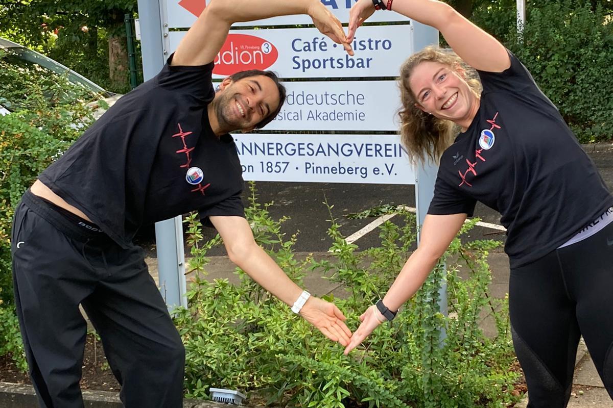 Zwei Personen bilden mit ihren H&auml;nden ein Herz vor einem Sportzentrumsschild in Pinneberg.
