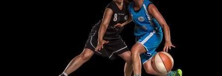 Zwei Basketballspielerinnen in Aktion, eine in schwarzer und eine in blauer Kleidung, dribbeln auf dem Spielfeld.
