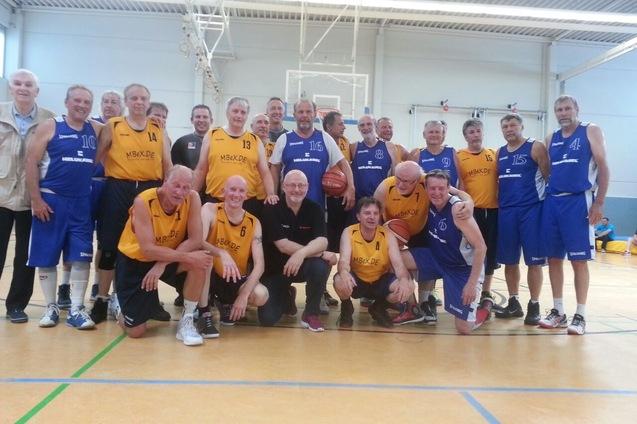 Gruppenfoto von &auml;lteren Basketballspielern in gelben und blauen Trikots in einer Sporthalle.