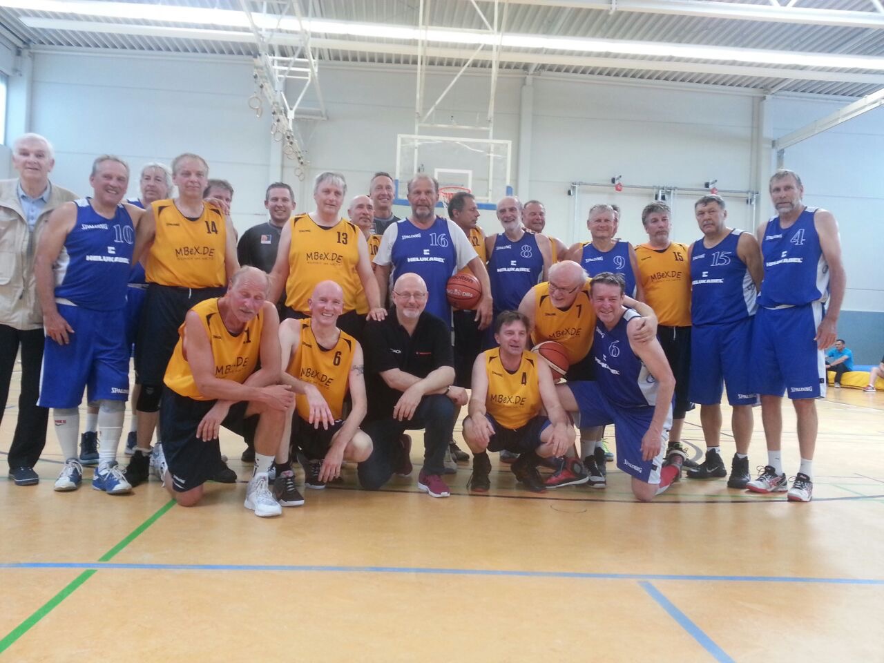 Gruppenfoto von älteren Basketballspielern in gelben und blauen Trikots in einer Sporthalle.