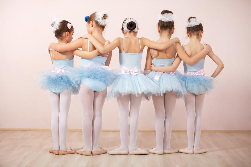 Fünf Ballettmädchen in blauen Tutus stehen Rücken an Rücken und halten sich gegenseitig um die Schultern.