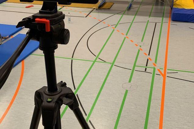 Auf einem Tischtennistraining sind ein Tisch, eine Kamera auf einem Stativ und ein Springer in der Luft zu sehen.