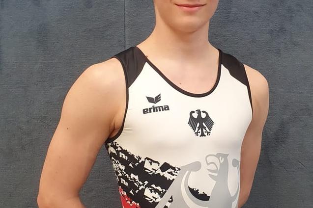 Junger Athlet in einem Sportanzug mit Deutschlands Farben, posiert vor einer neutralen Hintergrundwand.