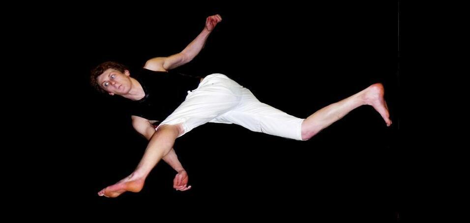 Zwei Akrobaten führen in der Luft synchron Sprünge aus, vor schwarzem Hintergrund, in sportlicher Kleidung.