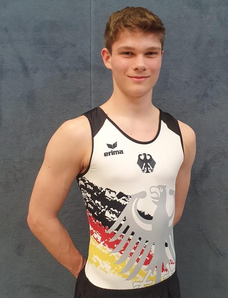 Junger Athlet in einem Sportanzug mit Deutschlands Farben, posiert vor einer neutralen Hintergrundwand.