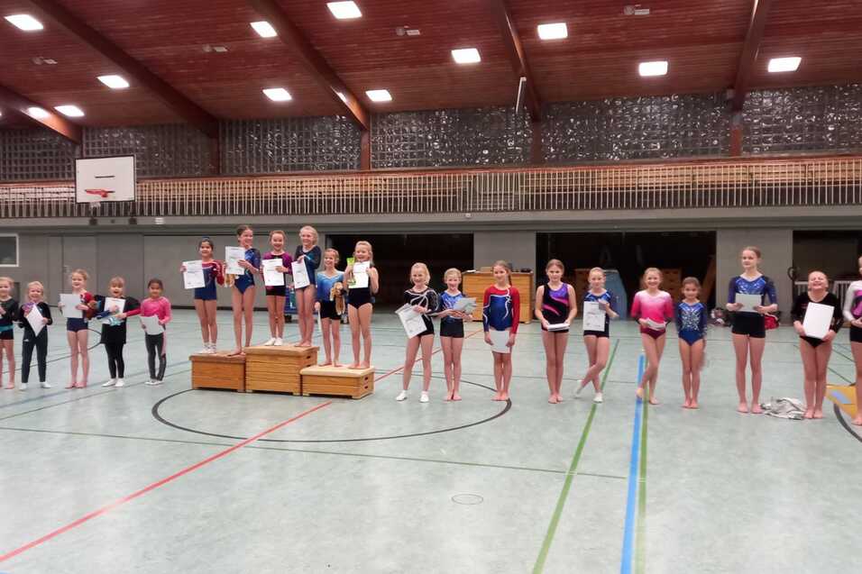 Gruppe junger Turnerinnen h&auml;lt Urkunden in einer Turnhalle, einige stehen auf einem Podest.