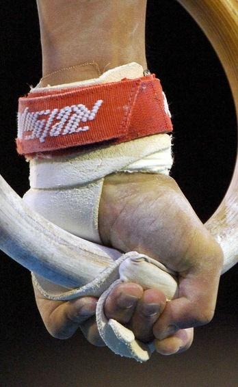 Nahaufnahme einer Hand, die einen Turnring mit weißem Material und einem roten Handgelenkband greift.