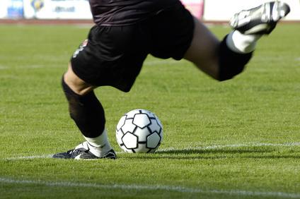 Nahaufnahme eines Fu&szlig;ballspielers, der einen Ball auf einem gr&uuml;nen Rasenfeld mit dynamischem Schuss ber&uuml;hrt.