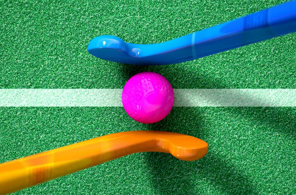 Bunte Hockeyschläger aus Blau und Orange umrahmen einen pinken Ball auf einer grünen Spielfläche mit weißem Streifen.