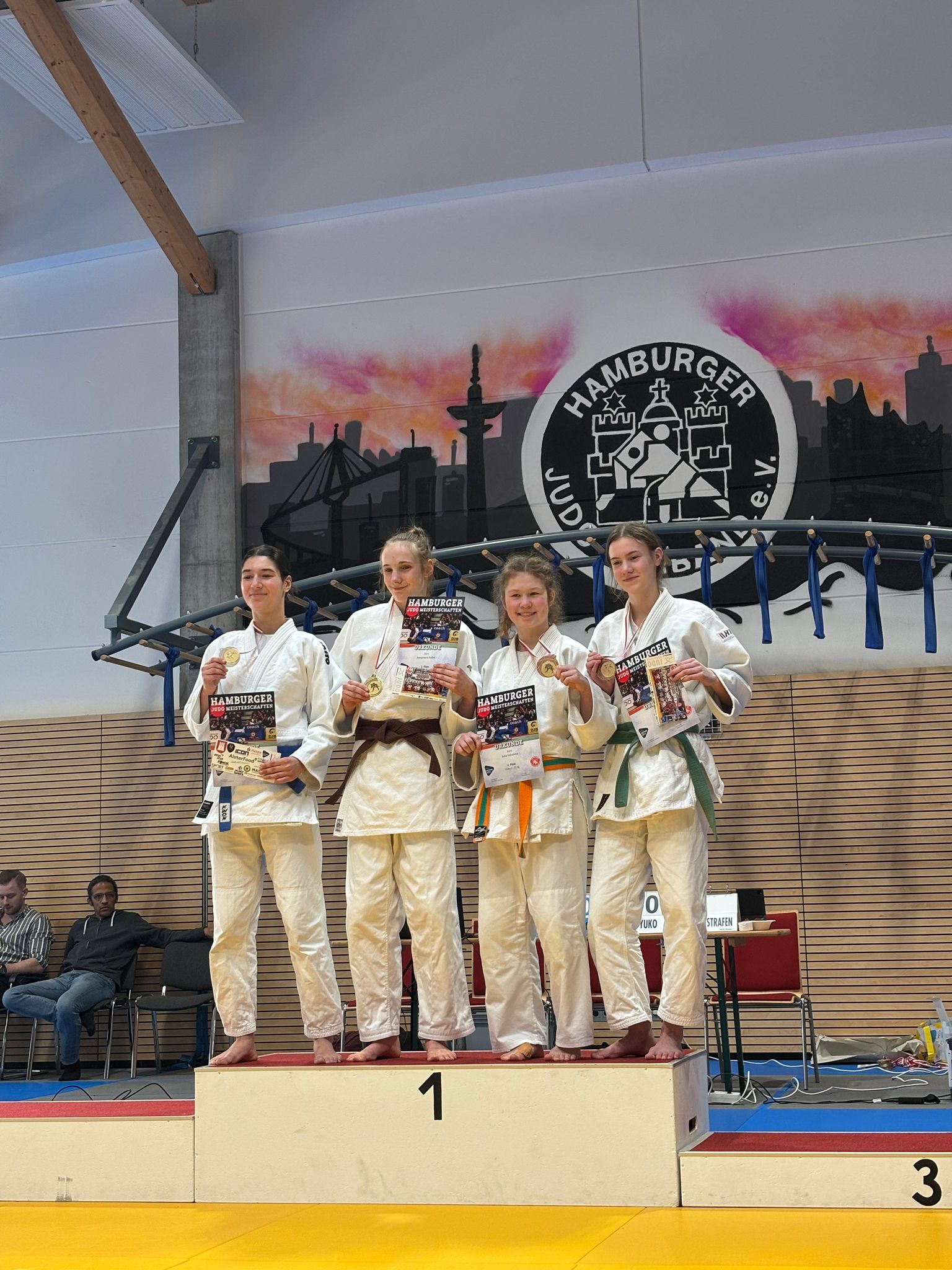 Vier Judoka stehen auf dem Siegertreppchen, halten Medaillen und Urkunden in der Sporthalle in Hamburg.