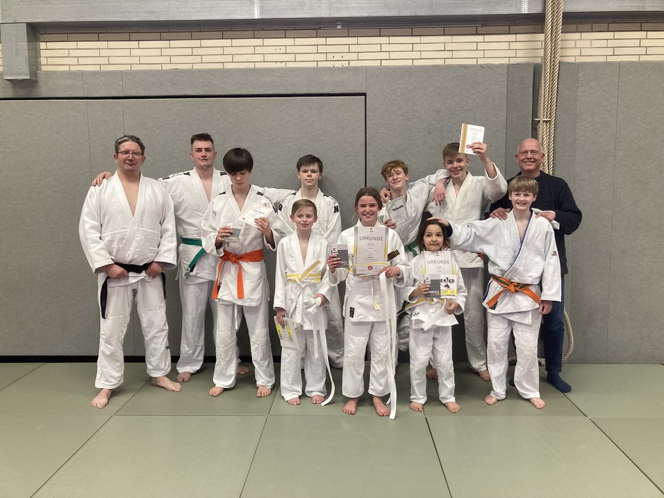 Gruppe von Judo-Praktizierenden in weißen Judogis mit Urkunden auf einer Judomatte.