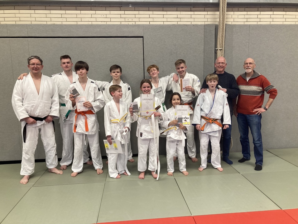 Gruppe von Judokas in weißen Anzügen mit Urkunden, posierend auf einer Tatami in einem Sportraum.