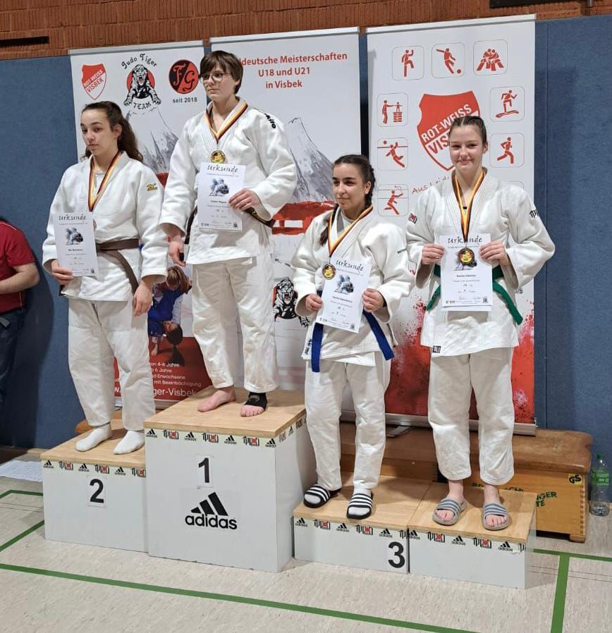 Vier Judokas stehen auf dem Siegerpodest, halten Urkunden und Medaillen in einer Sporthalle.