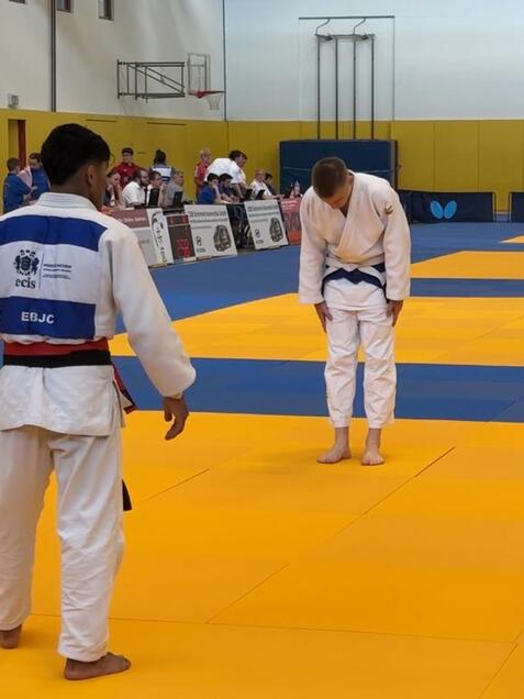 Zwei Judokas in einer Sporthalle, einer verbeugt sich auf der gelben Matte während der Wettkampf läuft.