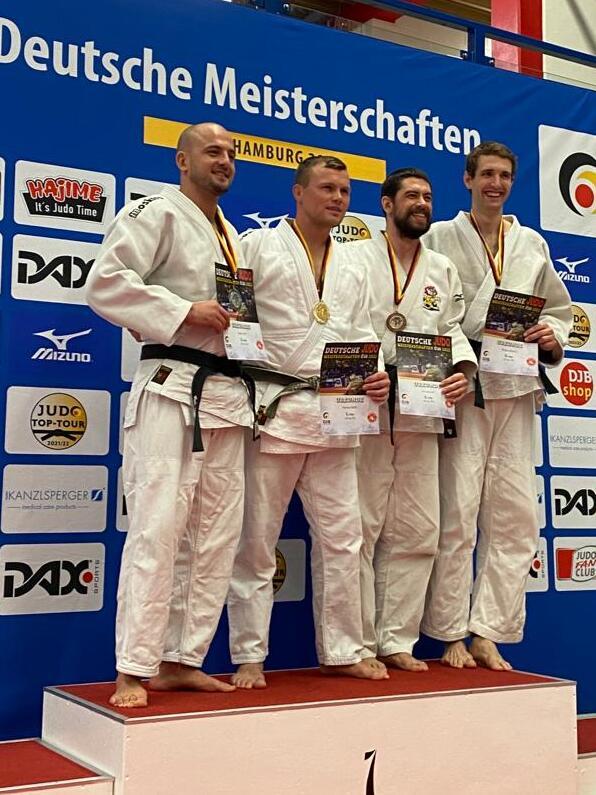 Vier Judoka in weißen Anzügen stehen auf dem Siegertreppchen der Deutschen Meisterschaften und halten Medaillen und Urkunden.