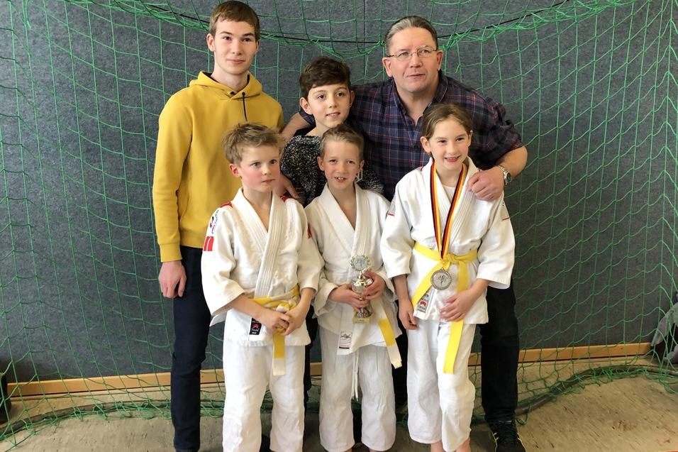 Gruppe von f&uuml;nf Personen, darunter Kinder in Judogis mit Medaillen, vor einem Netzhintergrund.