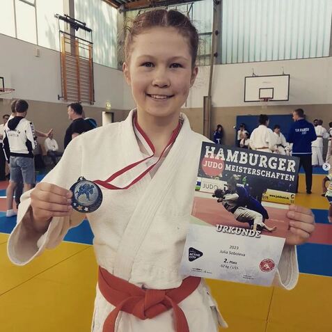 Junge Judoka in weißem Gi hält eine Medaille und ein Urkundenblatt für den zweiten Platz bei den Hamburger Meisterschaften.