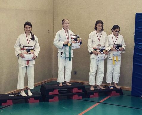 Vier junge Judoka stehen auf Treppchen und halten Siegerurkunden in der Hand, jeweils mit Medaillen um den Hals.