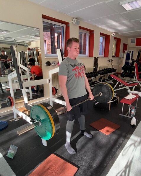 Junger Mann in Sportkleidung führt eine Deadlift-Übung mit einer Langhantel im Fitnessstudio aus.