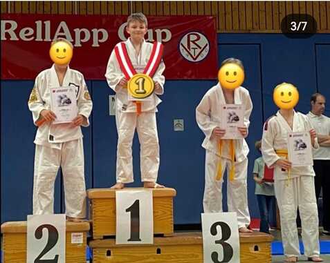 Drei Kinder in Judokleidung stehen auf dem Siegertreppchen beim RellApp Cup, jeder hält eine Urkunde.