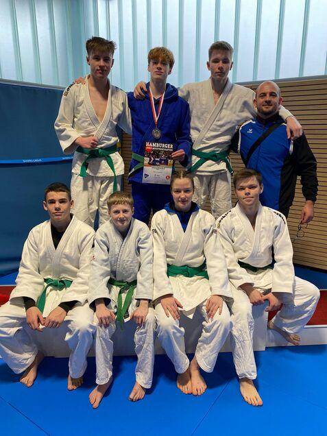 Gruppe von fünf Judokas in weißen und blauen Judoanzügen mit Medaille und Urkunde nach Wettkampf.