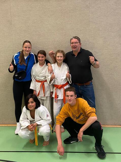 Gruppe von fünf Judo-Praktizierenden, lächelnd in Judokleidung, posieren vor einer neutralen Wand.