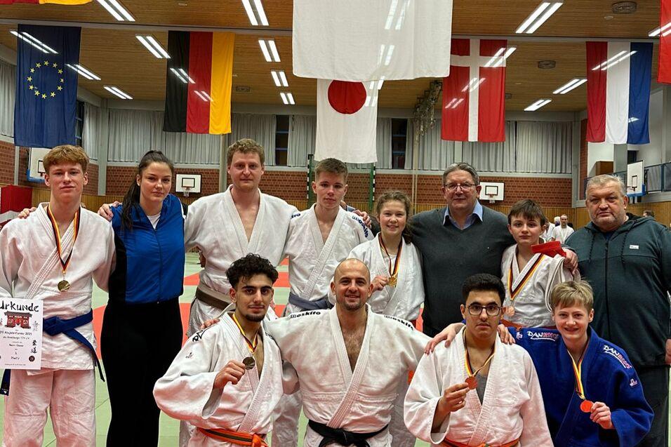Gruppe von Judoka mit Medaillen in der Sporthalle, umgeben von Flaggen und Matten. Urkunden in H&auml;nden eines Teilnehmers.