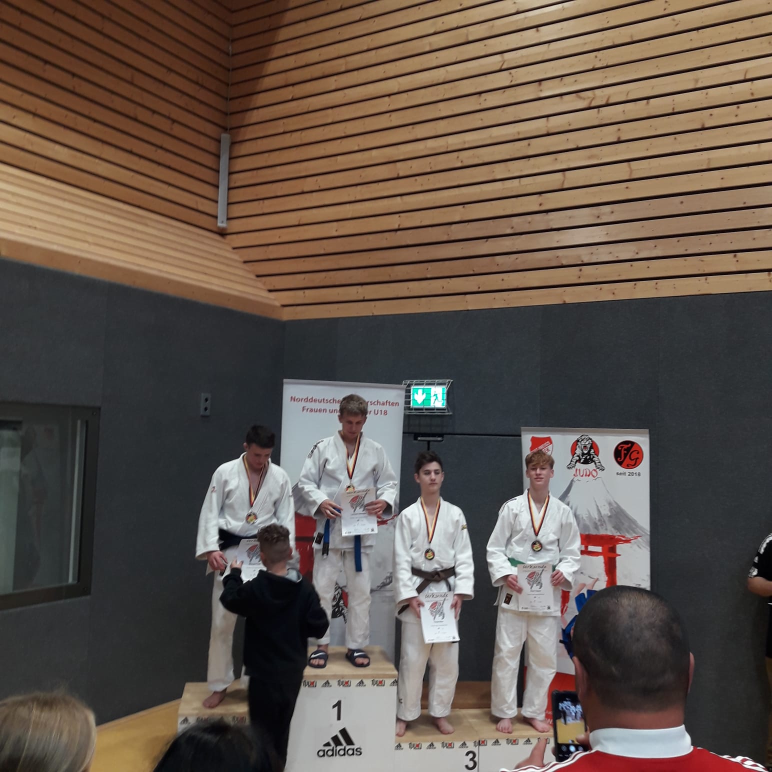 Junge Judoka stehen auf dem Siegerpodest mit Medaillen und Urkunden bei einem Wettkampf.