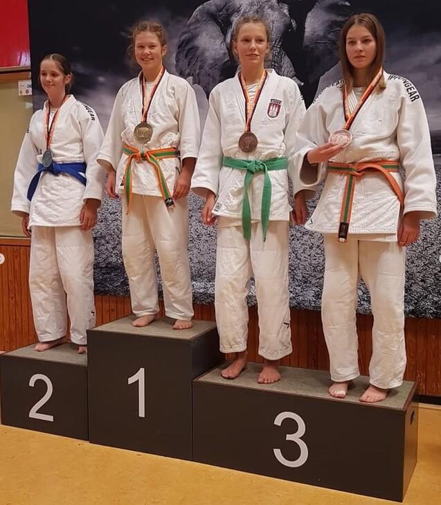 Vier Judoka mit Medaillen stehen auf dem Siegertreppchen, gekleidet in weiße Judo-Anzüge und unterschiedliche Gürtel.