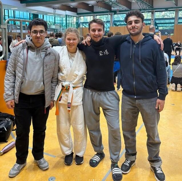 Gruppierung von vier Personen in Sportkleidung, darunter eine Judokämpferin, in einer Sporthalle.