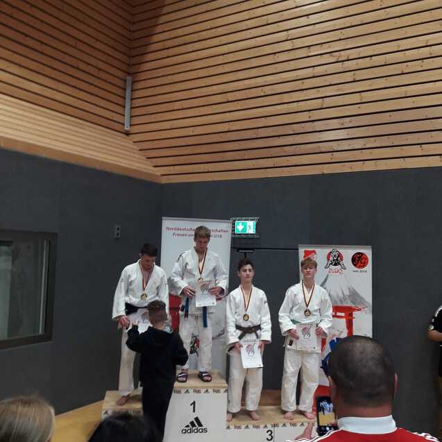 Junge Judoka stehen auf dem Siegerpodest mit Medaillen und Urkunden bei einem Wettkampf.