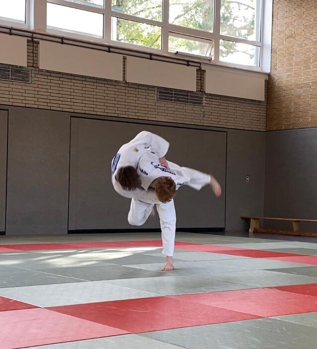 Sportler in Judokleidung führt einen Wurf im Training auf einer Judo-Matte aus, während er sich in der Luft befindet.