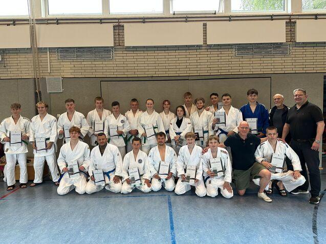 Gruppe von Judokas in weißen Anzügen, die stolz ihre Urkunden in einem Sportraum halten.