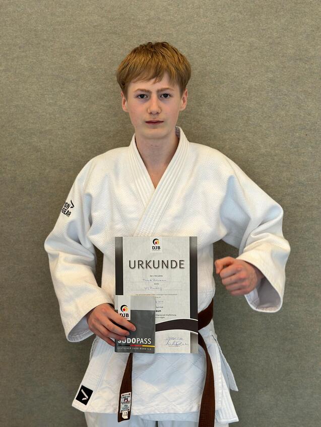 Jugendlicher in Judoanzug hält eine Urkunde und einen Judopass vor neutralem Hintergrund.